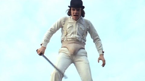 Alex looms over the camera, dressed in his bowler hat and all-white cricket attire, with the groin protector on the outside of his clothing. He wields a black baton, and looked frenzied and aggressive.